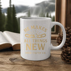 He Makes All Things New Mug (white ceramic) on a wooden table by a window with a Bible and pinecones – digital mockup