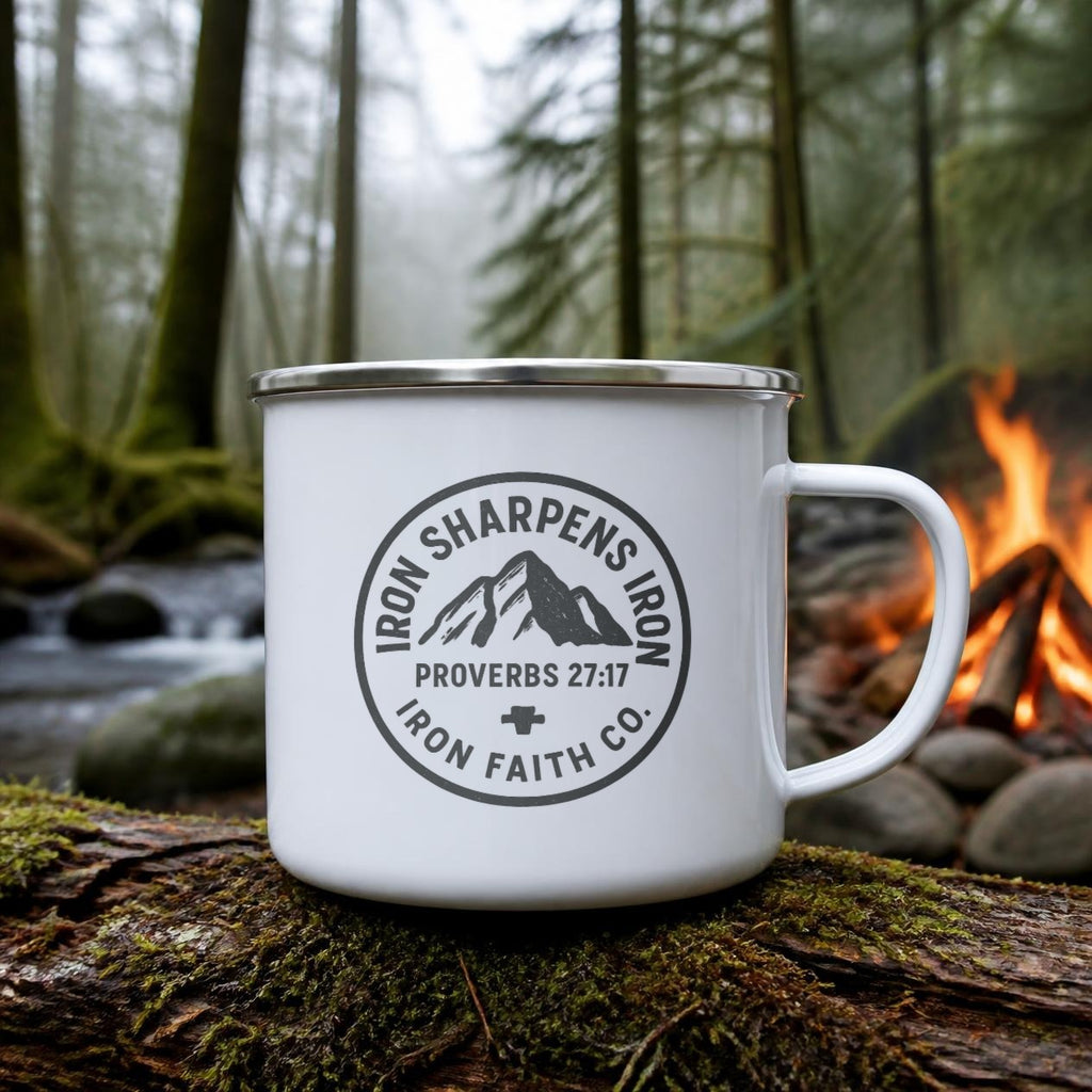 Iron Sharpens Iron Enamel Camp Mug (white enamel) on a mossy log beside a campfire – digital mockup