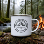 Iron Sharpens Iron Enamel Camp Mug (white enamel) on a mossy log beside a campfire – digital mockup