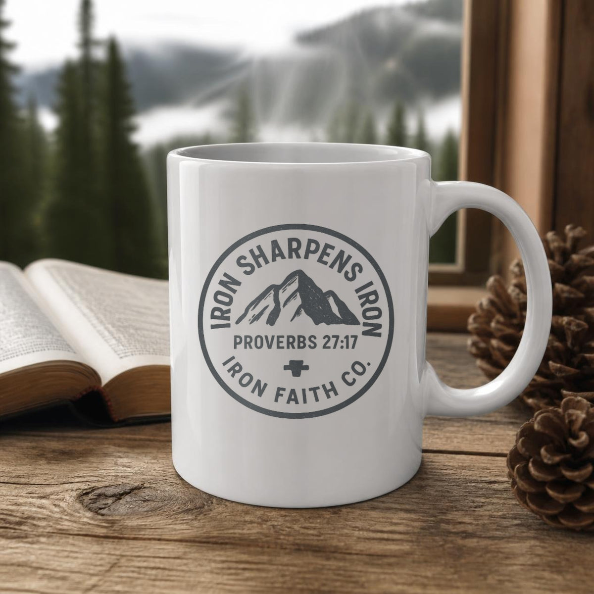 Iron Sharpens Iron Mug (white ceramic) on a wooden table by a window with a Bible and pinecones – digital mockup