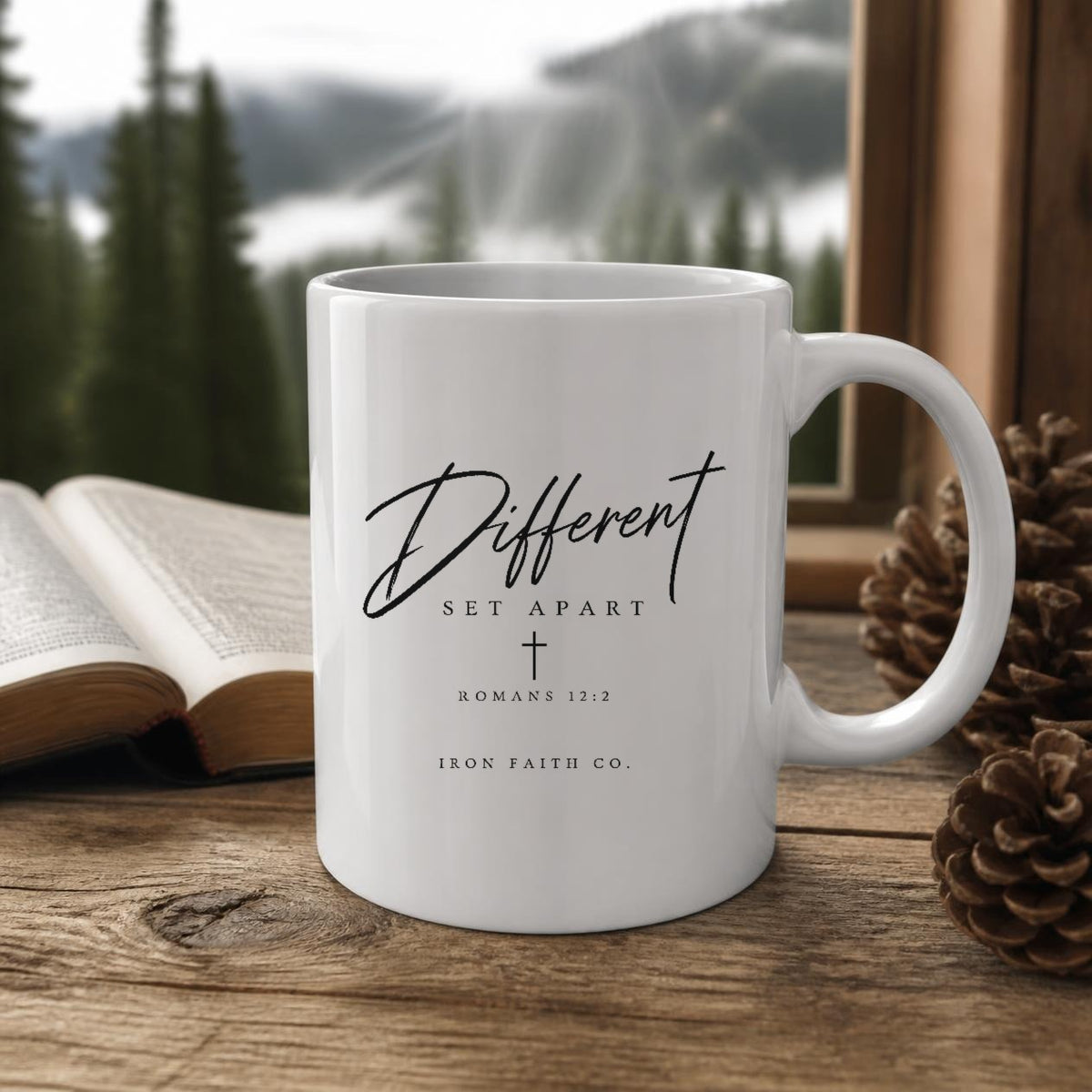 The Different Romans 12:2 Mug (11oz, white) on a wooden cabin table with an open Bible and pine cones (digitally composited scene image)