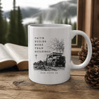 The Faith Builds More Than Buildings Mug (11oz, white) on a wooden cabin table with an open Bible and pine cones (digitally composited scene image)