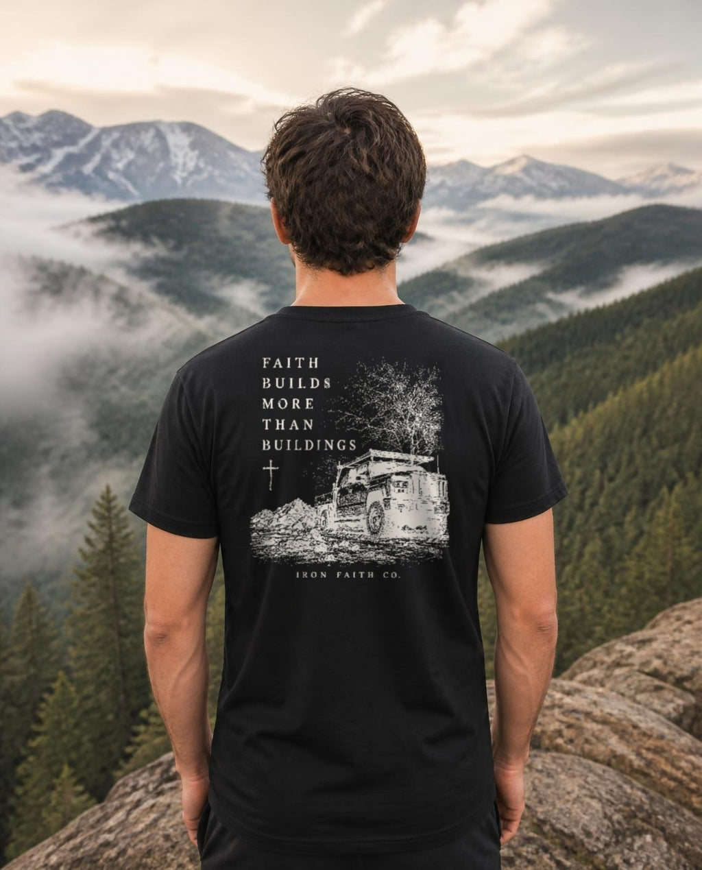 Fictional model wearing the Faith Builds More Than Buildings Tee – Back Print in Black, back view, Pacific Northwest scene (digitally composited lifestyle image)