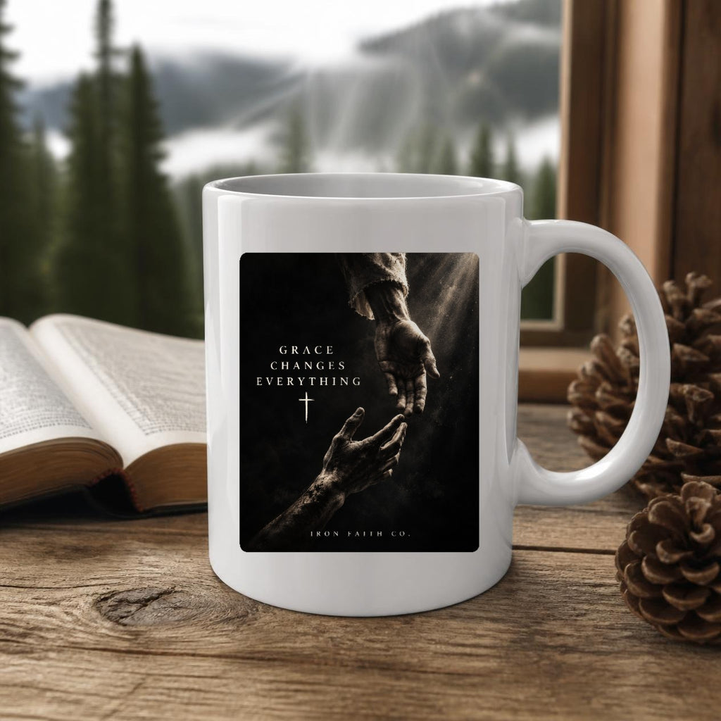 The Grace Changes Everything Mug (11oz, white) on a wooden cabin table with an open Bible and pine cones (digitally composited scene image)