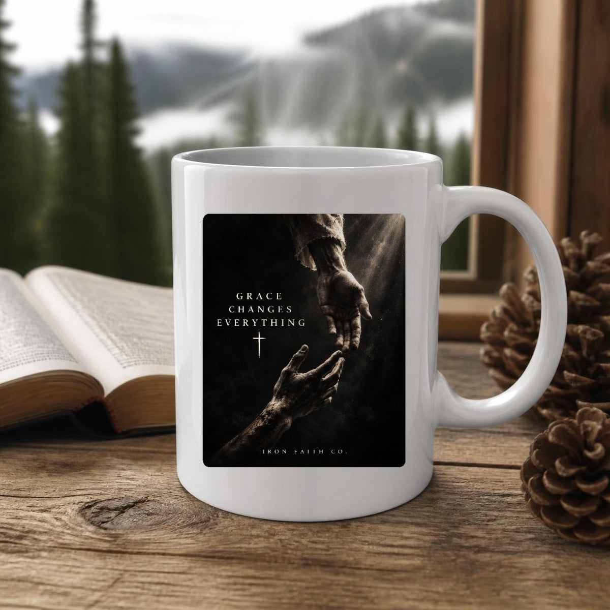 The Grace Changes Everything Mug (11oz, white) on a wooden cabin table with an open Bible and pine cones (digitally composited scene image)