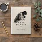 The Pray Harder Hardcover Journal on a wooden table with coffee, a pen and a pine cone (digitally composited scene image)
