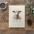 The Worthy Revelation 5:12 Hardcover Journal on a wooden table with coffee, a pen and a pine cone (digitally composited scene image)