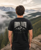 Fictional model wearing the Built on a Higher Standard Tee – Back Print in Black, back view, Pacific Northwest scene (digitally composited lifestyle image)