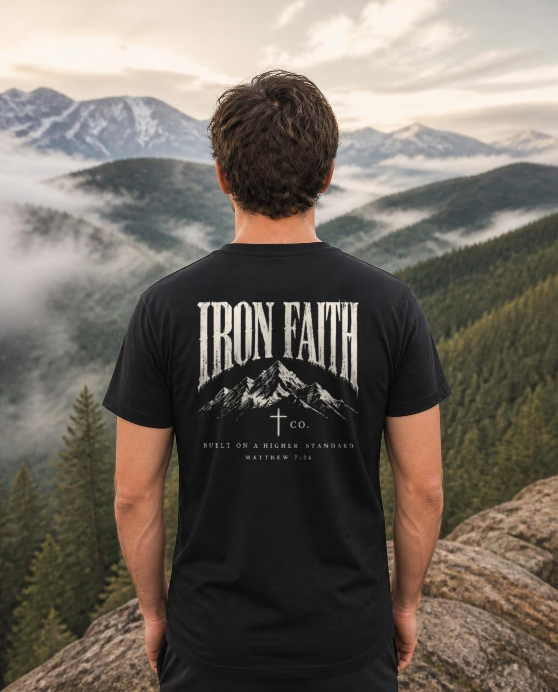 Fictional model wearing the Built on a Higher Standard Tee – Back Print in Black, back view, Pacific Northwest scene (digitally composited lifestyle image)