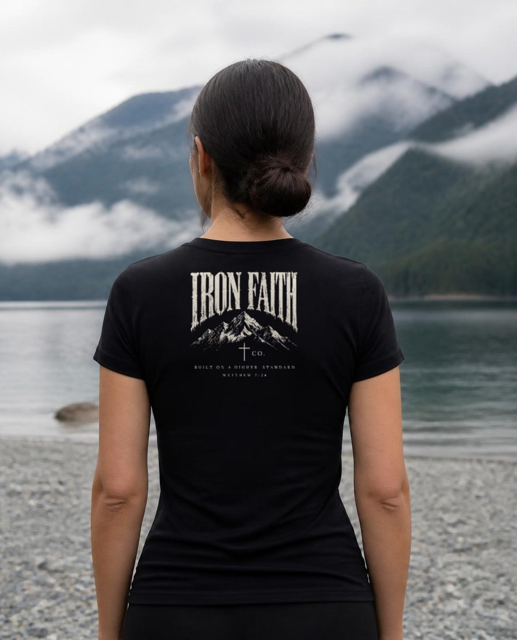 Fictional model wearing the Built on a Higher Standard Women's Fitted Tee – Back Print in Black, back view, Pacific Northwest scene (digitally composited lifestyle image)