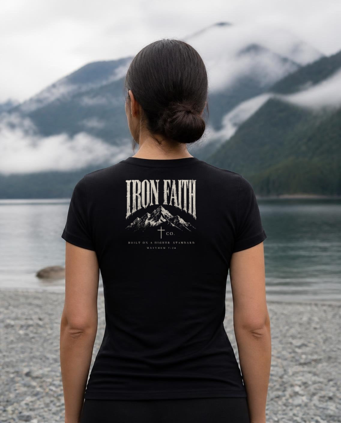 Fictional model wearing the Built on a Higher Standard Women's Fitted Tee – Back Print in Black, back view, Pacific Northwest scene (digitally composited lifestyle image)