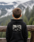 Fictional model wearing the Built on a Higher Standard Youth Hoodie – Back Print in Black, back view, Pacific Northwest scene (digitally composited lifestyle image)