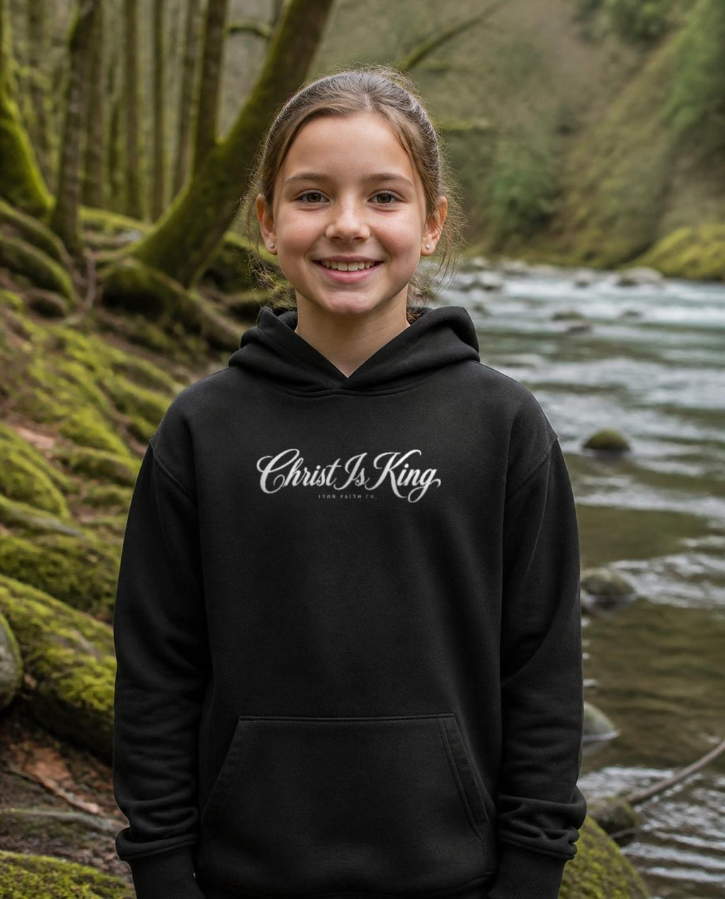 Fictional model wearing the Christ Is King Youth Hoodie in Black, Pacific Northwest scene (digitally composited lifestyle image)
