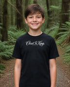 Fictional model wearing the Christ Is King Youth Tee in Black, Pacific Northwest scene (digitally composited lifestyle image)
