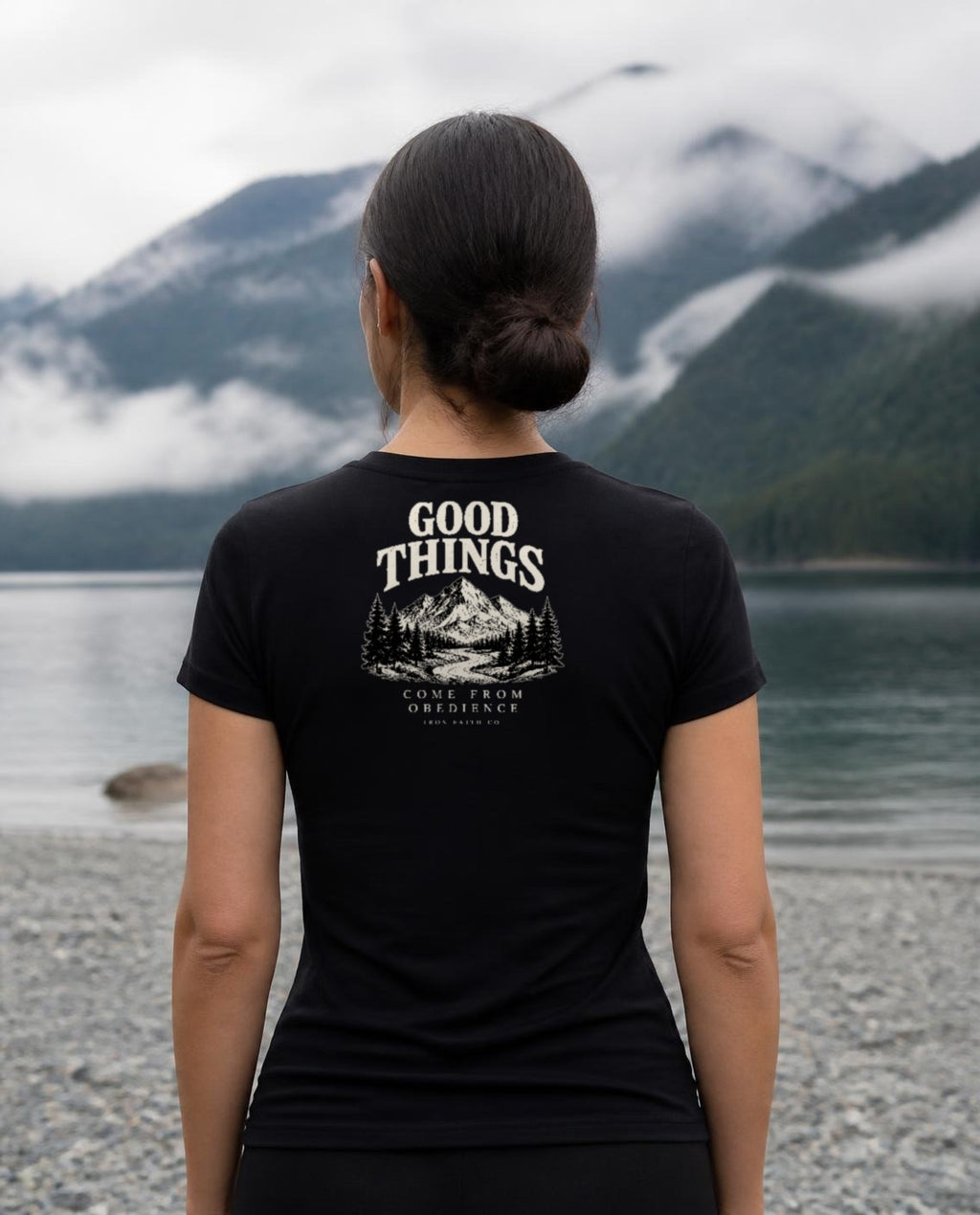 Fictional model wearing the Good Things Come From Obedience Women's Fitted Tee – Back Print in Black, back view, Pacific Northwest scene (digitally composited lifestyle image)