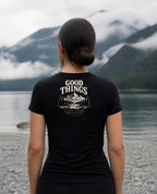 Fictional model wearing the Good Things Come From Obedience Women's Fitted Tee – Back Print in Black, back view, Pacific Northwest scene (digitally composited lifestyle image)