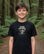 Fictional model wearing the Good Things Come From Obedience Youth Tee in Black, Pacific Northwest scene (digitally composited lifestyle image)
