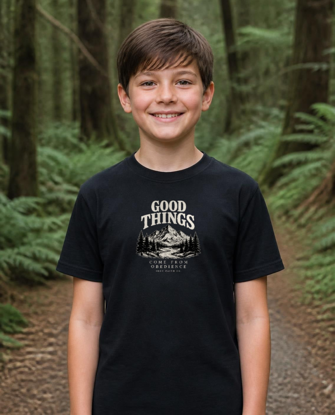 Fictional model wearing the Good Things Come From Obedience Youth Tee in Black, Pacific Northwest scene (digitally composited lifestyle image)