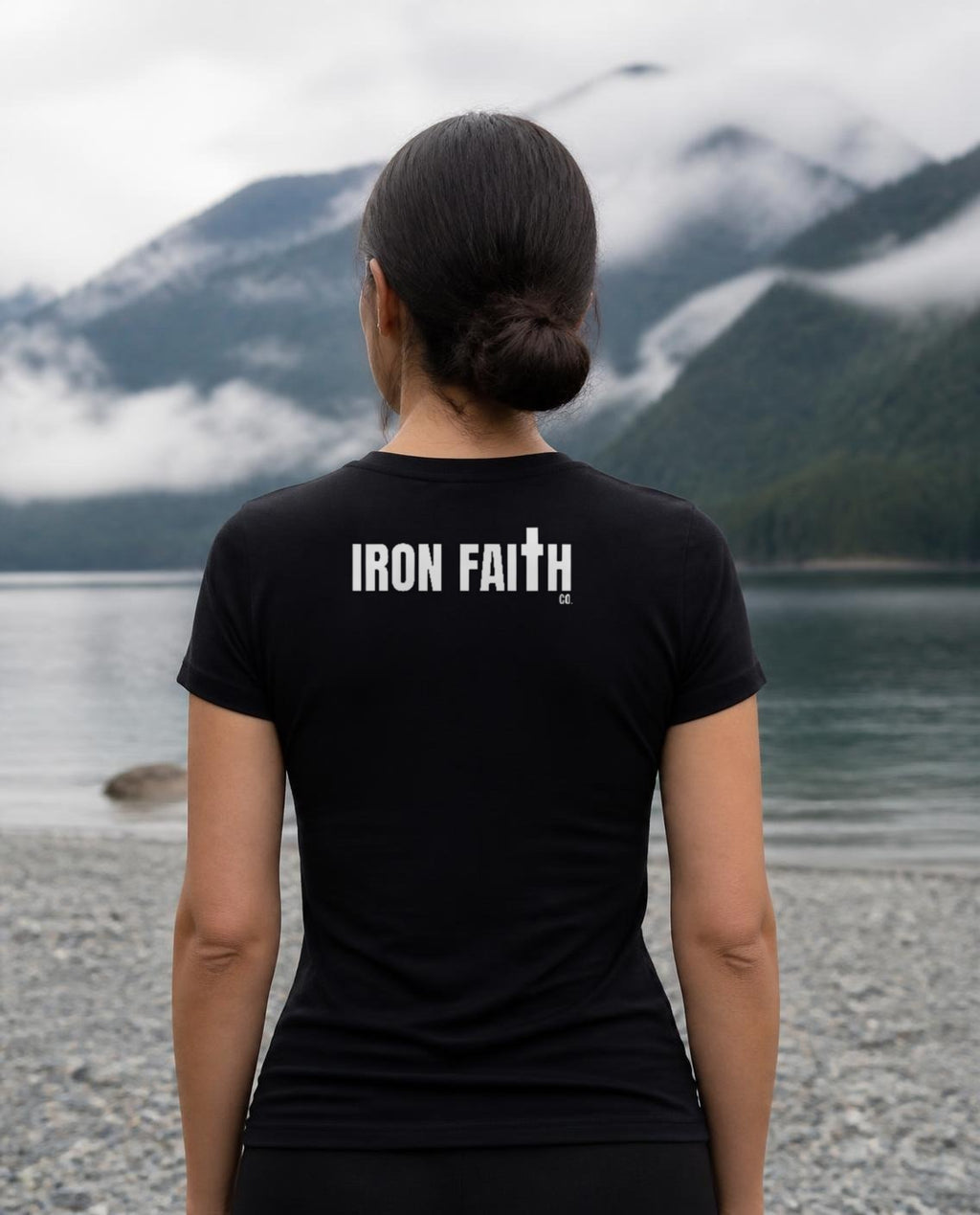 Fictional model wearing the Iron Faith Co. Wordmark Women's Fitted Tee – Back Print in Black, back view, Pacific Northwest scene (digitally composited lifestyle image)