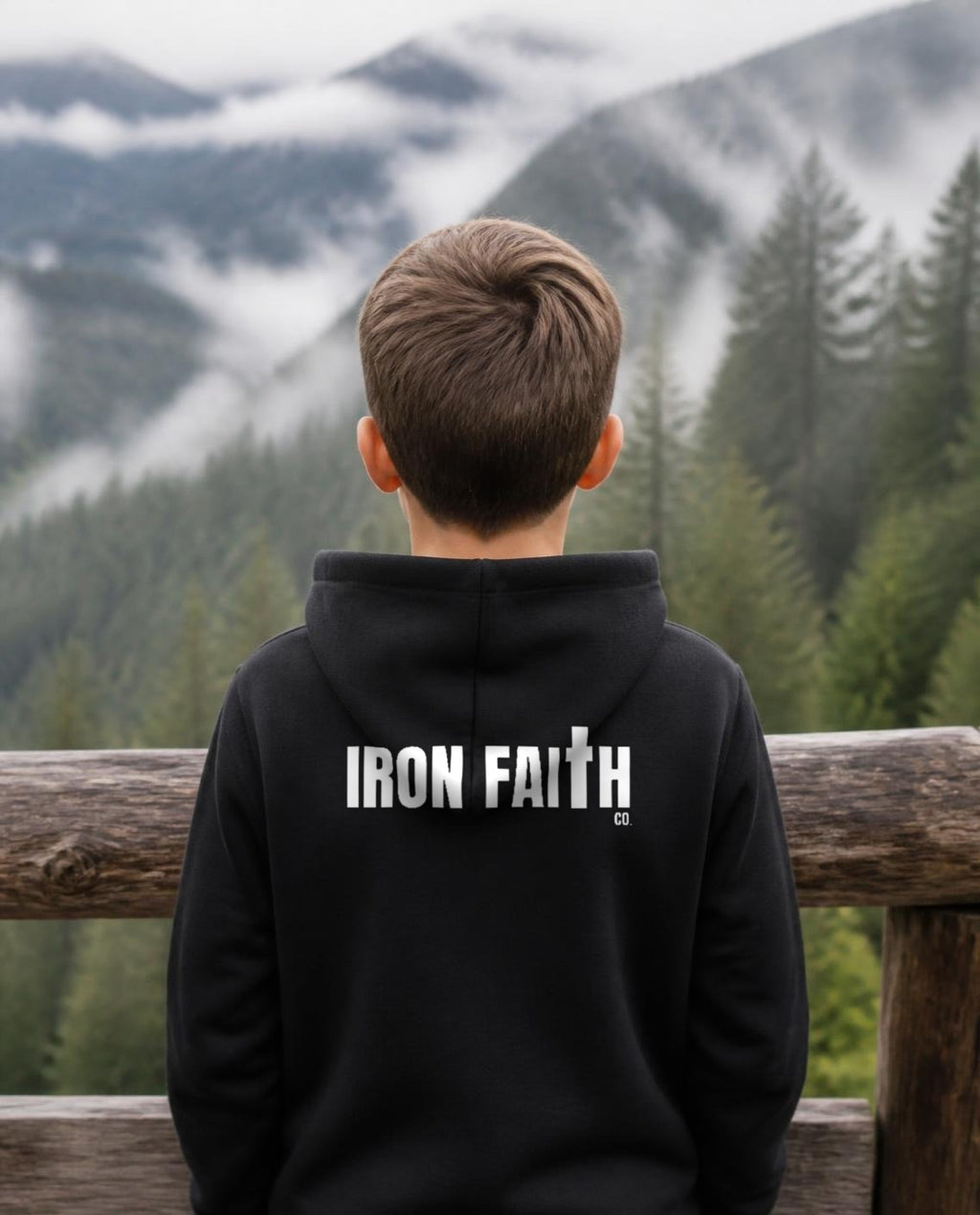 Fictional model wearing the Iron Faith Co. Wordmark Youth Hoodie – Back Print in Black, back view, Pacific Northwest scene (digitally composited lifestyle image)