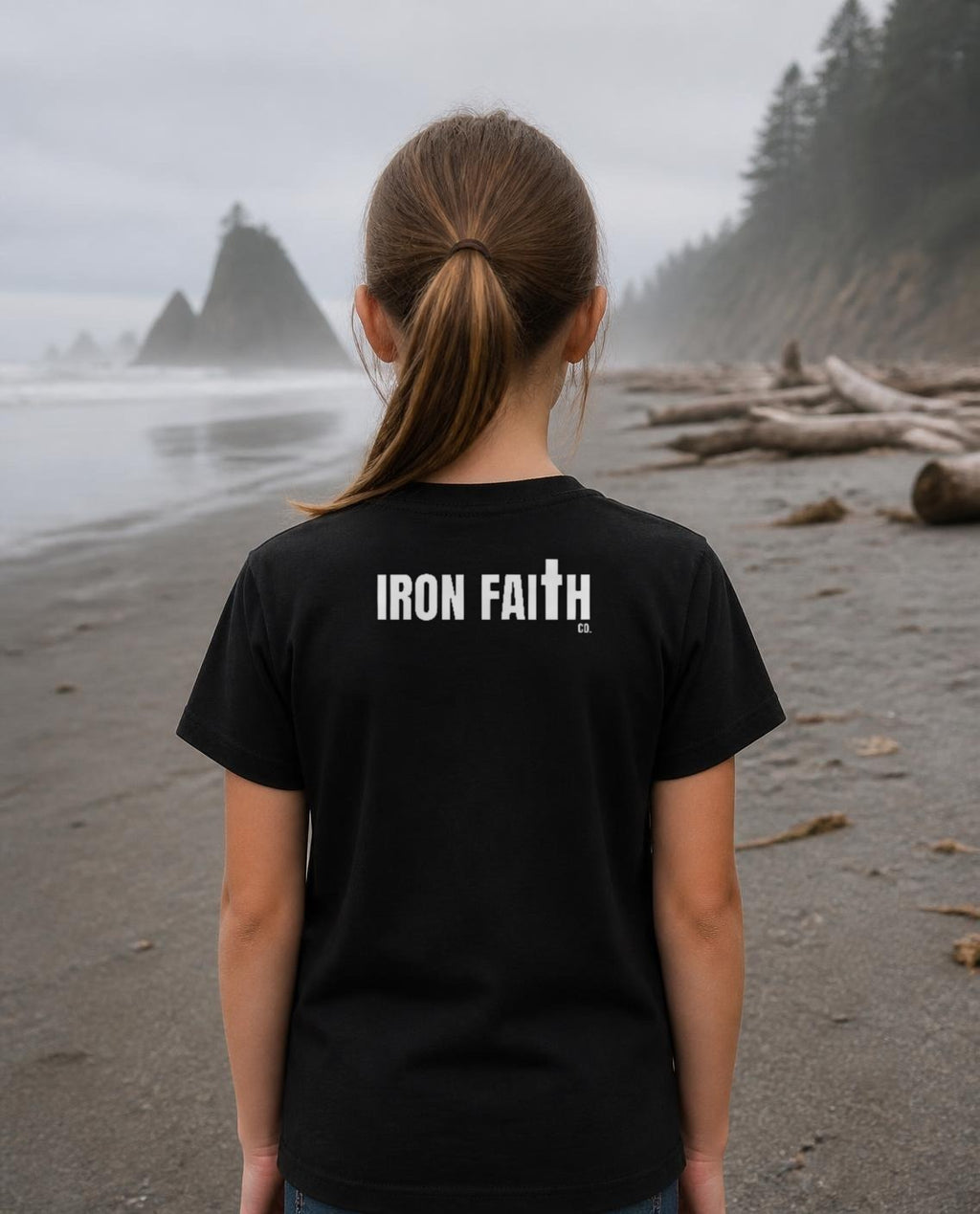 Fictional model wearing the Iron Faith Co. Wordmark Youth Tee – Back Print in Black, back view, Pacific Northwest scene (digitally composited lifestyle image)