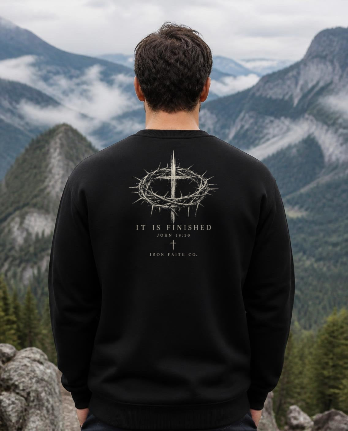 Fictional model wearing the It Is Finished Crewneck in Black, back view, Pacific Northwest scene (digitally composited lifestyle image)
