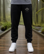 Fictional model wearing the It Is Finished Sweatpants in Black, Pacific Northwest scene (digitally composited lifestyle image)