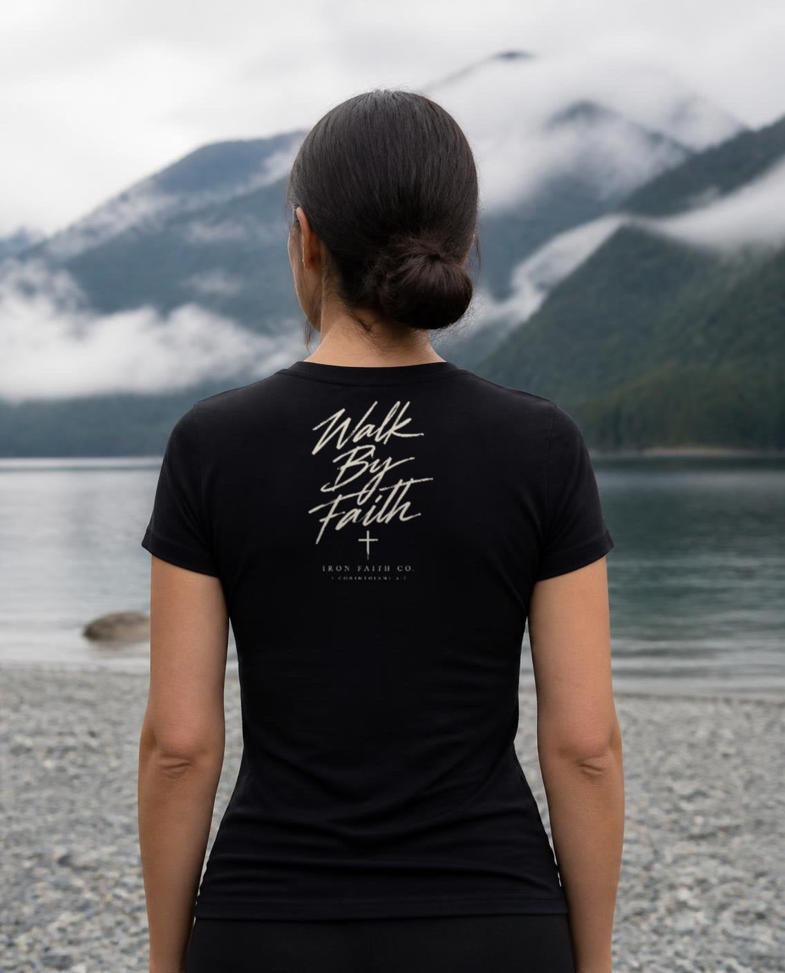 Fictional model wearing the Walk By Faith Women's Fitted Tee – Back Print in Black, back view, Pacific Northwest scene (digitally composited lifestyle image)