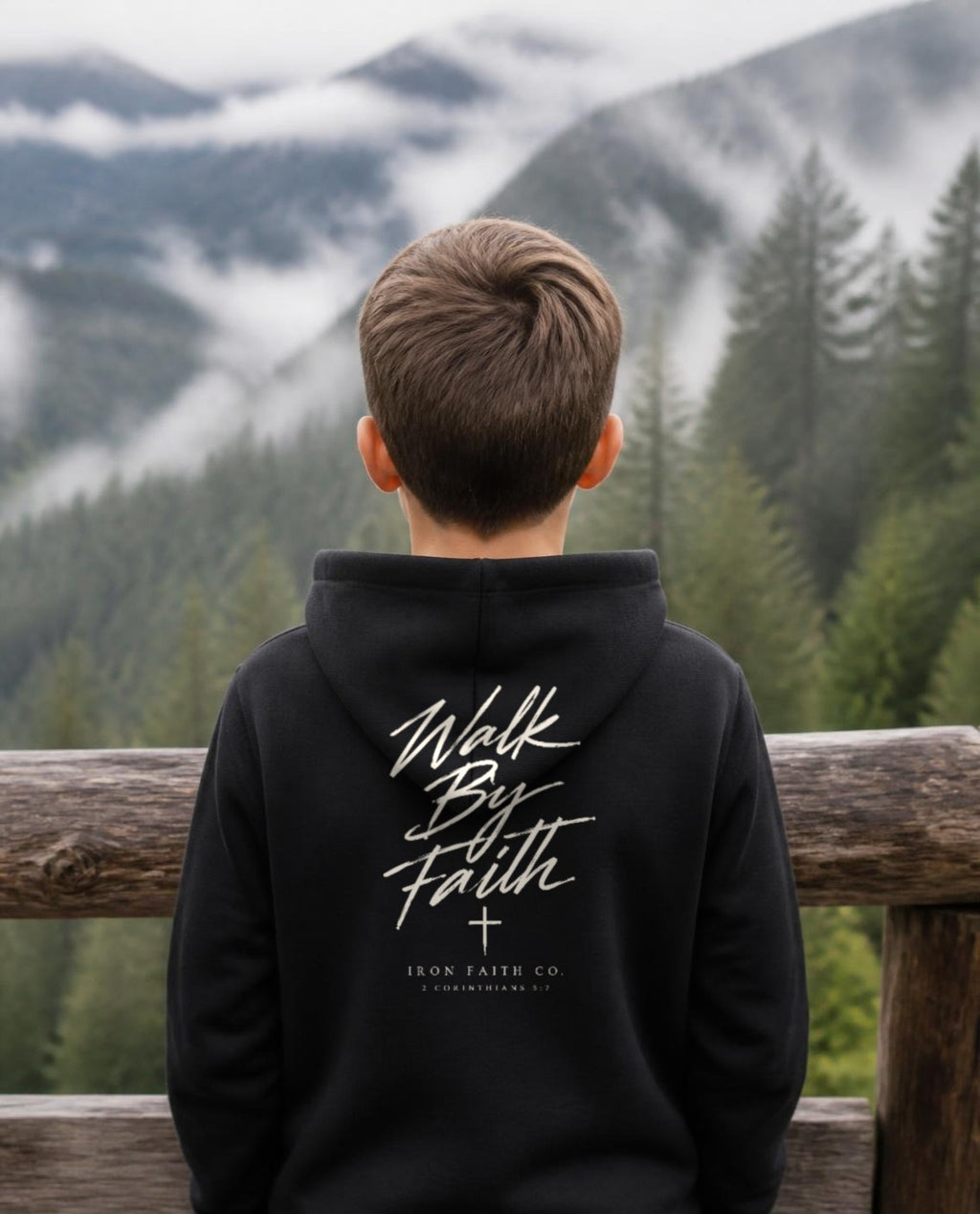 Fictional model wearing the Walk By Faith Youth Hoodie – Back Print in Black, back view, Pacific Northwest scene (digitally composited lifestyle image)