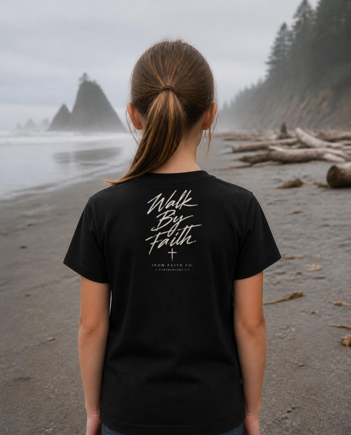 Fictional model wearing the Walk By Faith Youth Tee – Back Print in Black, back view, Pacific Northwest scene (digitally composited lifestyle image)