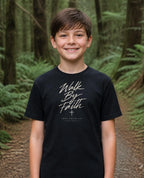Fictional model wearing the Walk By Faith Youth Tee in Black, Pacific Northwest scene (digitally composited lifestyle image)