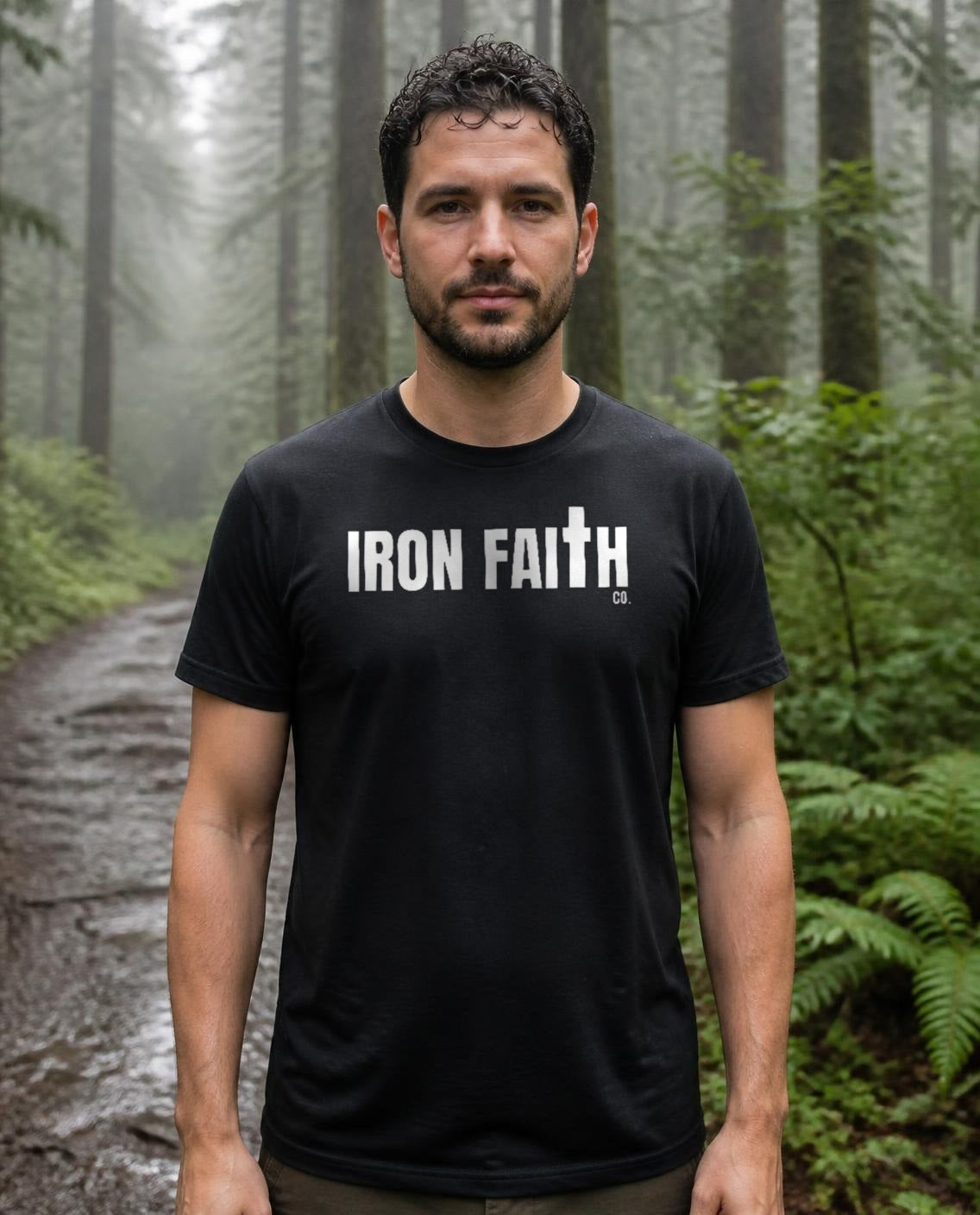 Fictional model wearing the Iron Faith Co. Wordmark Tee in Black, Pacific Northwest forest trail (digitally composited lifestyle image)