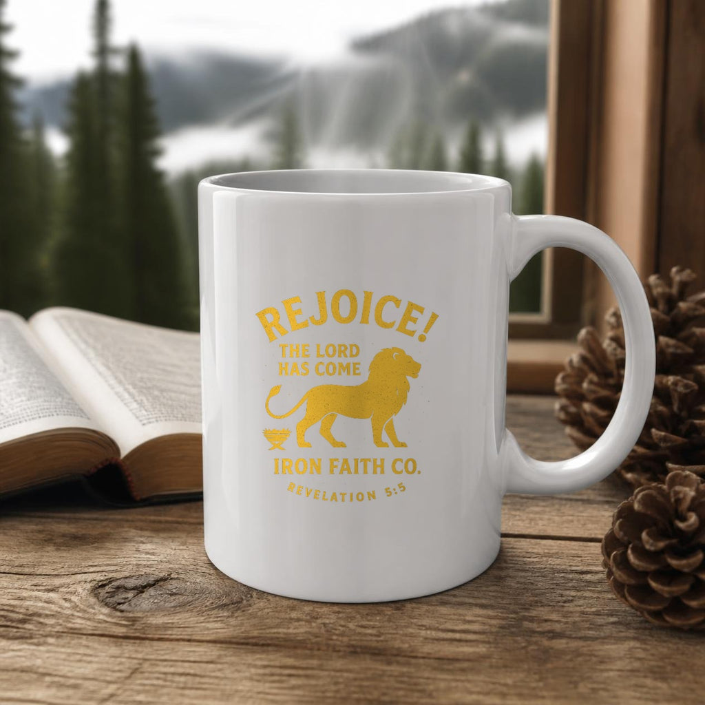 Rejoice! The Lord Has Come Mug (white ceramic) on a wooden table by a window with a Bible and pinecones – digital mockup