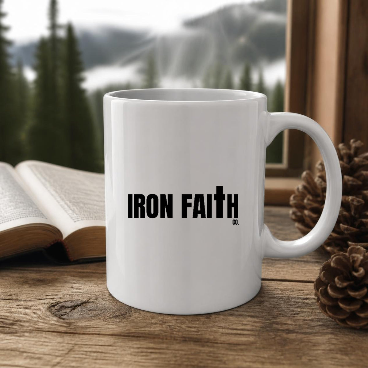 Iron Faith Co. Wordmark Mug (white ceramic) on a wooden table by a window with a Bible and pinecones – digital mockup